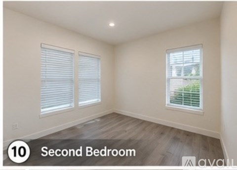 A second bedroom with wood flooring and a window with blinds.