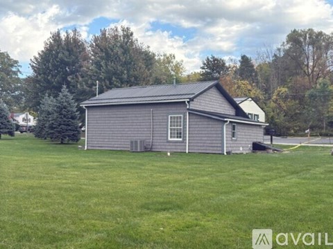 A small house with a grey roof is surrounded by a grassy field.