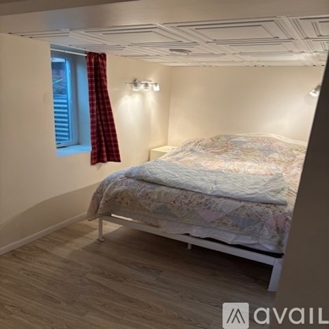 A bedroom with a bed, a window with a red curtain, and a wooden floor.