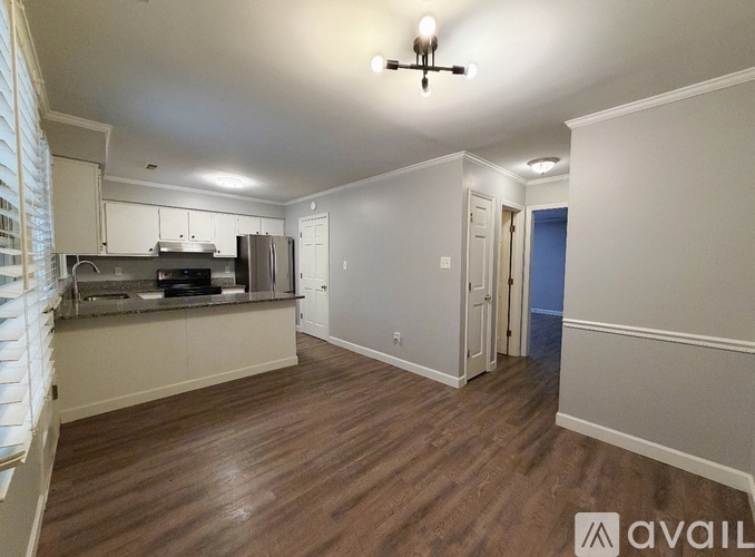 A room with wooden floors and a kitchen area with white cabinets and a stove top oven.