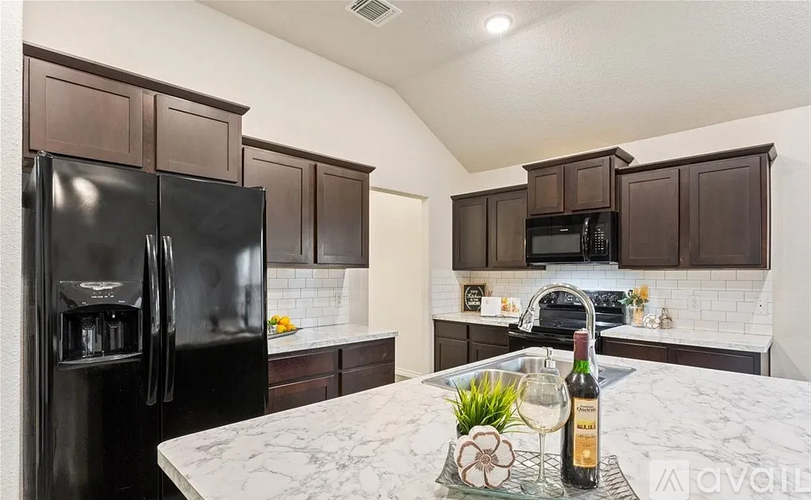 A kitchen with a black fridge and brown cabinets.