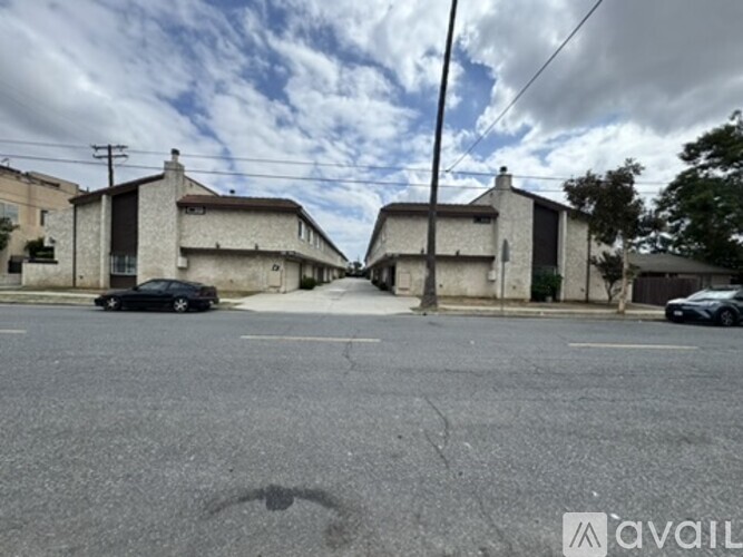 A black car is parked on the left side of a street with buildings on both sides.
