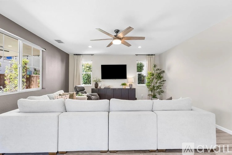 A white couch is in the middle of a living room with a ceiling fan and a television.