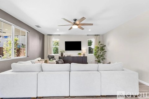 A white couch is in the middle of a living room with a ceiling fan and a television.
