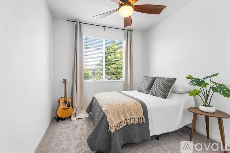 A bedroom with a bed, a guitar, a ceiling fan, and a potted plant.