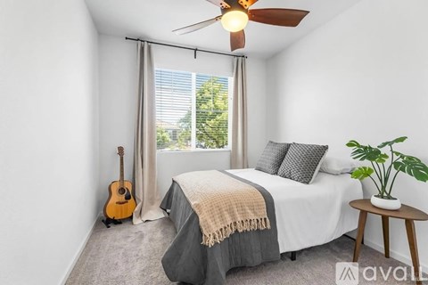 A bedroom with a bed, a guitar, a ceiling fan, and a potted plant.