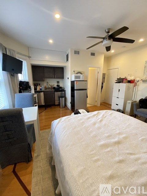 A bedroom with a large bed and a kitchen area in the background.