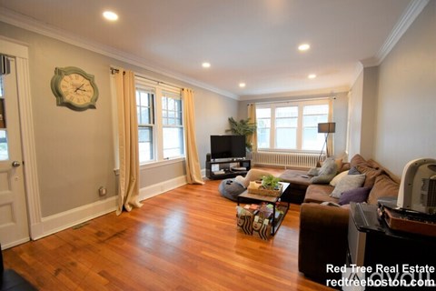 A living room with a wooden floor and a large clock on the wall.