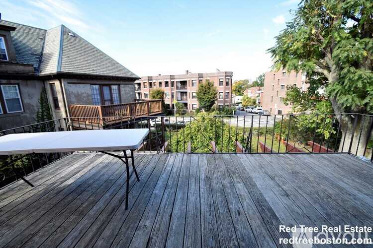 A wooden deck with a white table and chairs is in the foreground with apartment buildings in the background.