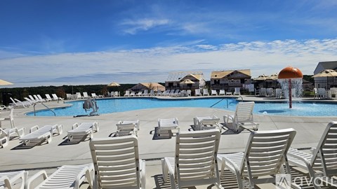 A pool with sun loungers in the foreground and a building in the background.
