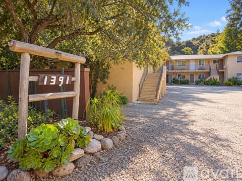 A wooden sign with the number 1391 is in front of a building with a gravel driveway and landscaping.