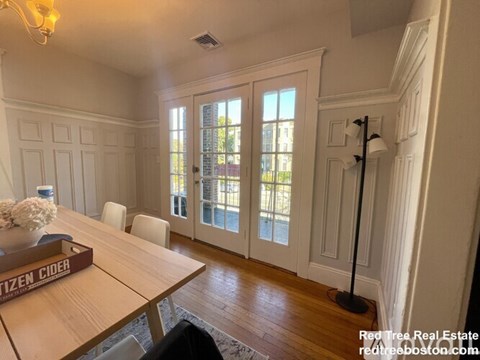 A dining room with a wooden table and chairs and a vase of flowers on it.