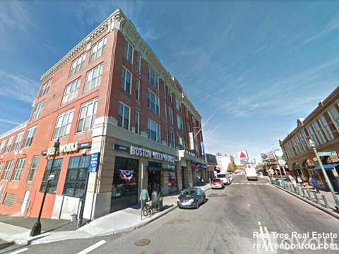 A street view of a city with a building on the left and a car driving on the road.