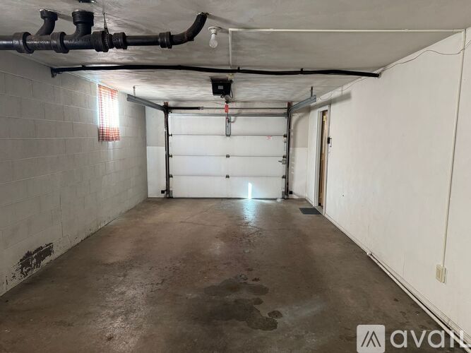 A spacious garage with a concrete floor and white walls, featuring a white garage door and a red light on the ceiling.