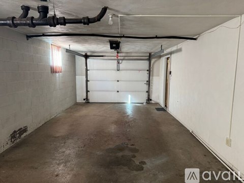 A spacious garage with a concrete floor and white walls, featuring a white garage door and a red light on the ceiling.