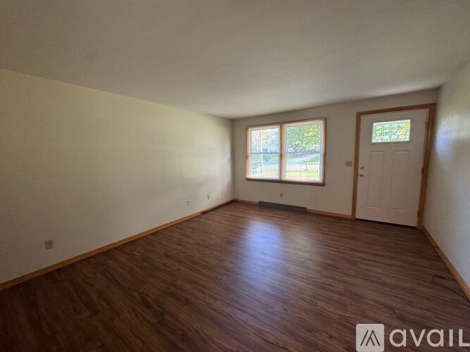 A room with wooden flooring and a window with a view of trees.