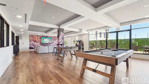 A pool table is in the middle of a room with wood floors and a high ceiling.
