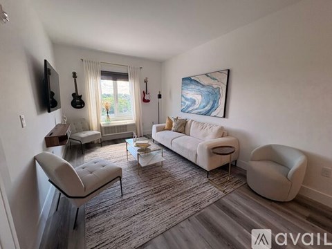 A living room with a white couch, a chair, a coffee table, and a painting on the wall.