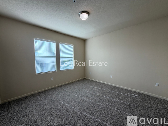 A spacious room with carpeted floor and two windows.