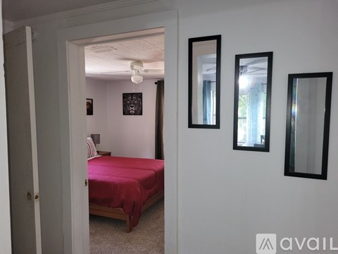A bedroom with a red bedspread and a mirror on the wall.