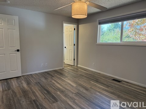 A room with a wooden floor and a window with a view of trees outside.