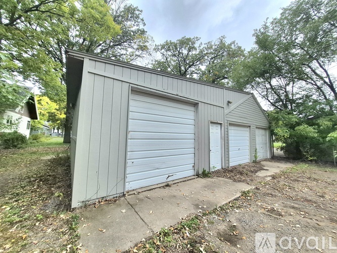 A grey garage with a closed white door is surrounded by trees.