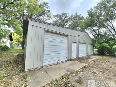 A grey garage with a closed white door is surrounded by trees.