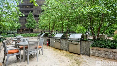 A patio with a table and chairs is surrounded by trees and a building.