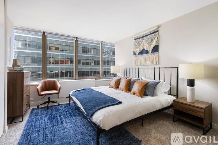 A bedroom with a large bed, a chair, and a window overlooking a building.