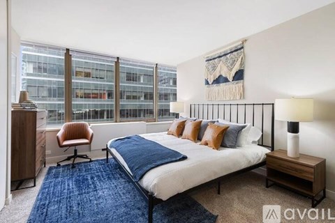 A bedroom with a large bed, a chair, and a window overlooking a building.