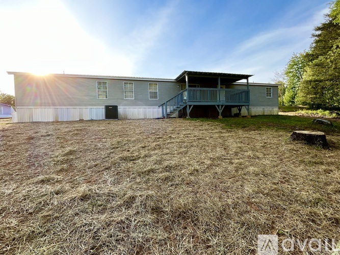 A large metal building with a porch and a garage door is surrounded by a grassy field.