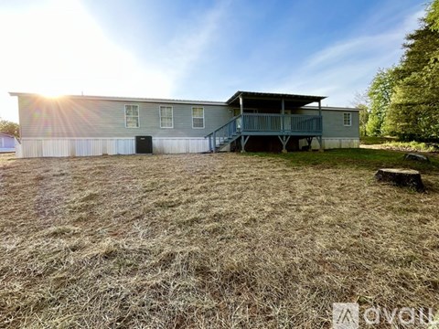 A large metal building with a porch and a garage door is surrounded by a grassy field.