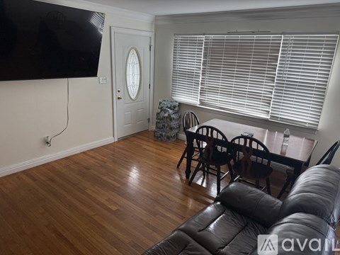 A living room with a black leather couch and a flat screen TV mounted on the wall.