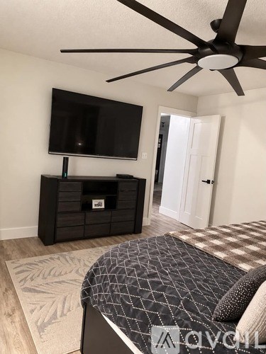 A bedroom with a bed, a television, and a ceiling fan.
