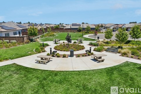 A park area with picnic tables and a fountain in the middle of a grassy circle.