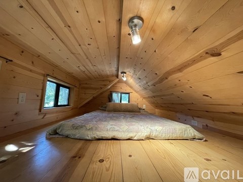 A bedroom with wooden walls and ceiling, a bed in the center, and a light bulb hanging from the ceiling.