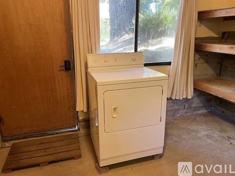 A white cabinet with a door and a drawer is in a room with a wooden floor and a window.