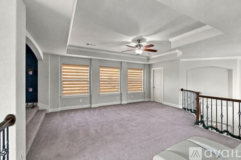A spacious room with a ceiling fan and light, carpeted floor, and a staircase with a railing.