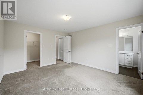 A spacious room with a carpeted floor and white walls, with a small white cabinet and a single door visible.