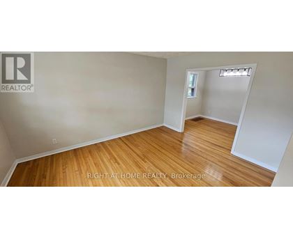 A room with wooden flooring and white walls, with a small window and a doorway leading to another room.