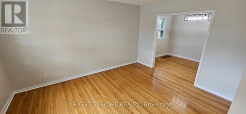 A room with wooden flooring and white walls, with a small window and a doorway leading to another room.