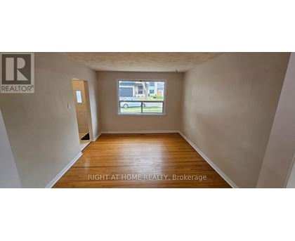 A room with wooden floors and a window showing a parking lot outside.