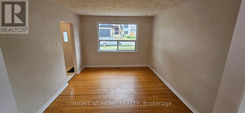A room with wooden floors and a window showing a parking lot outside.