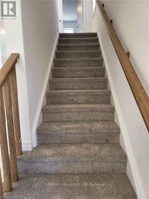 A staircase with a wooden handrail and carpeted steps.
