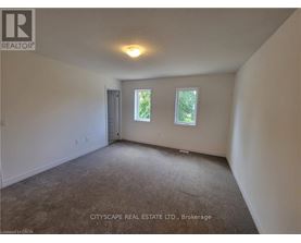 A spacious room with a carpeted floor, a ceiling light, and a window showing greenery outside.