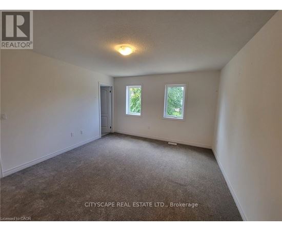A spacious room with a carpeted floor, a ceiling light, and a window showing greenery outside.