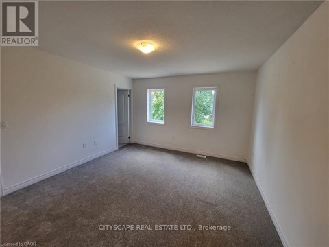 A spacious room with a carpeted floor, a ceiling light, and a window showing greenery outside.