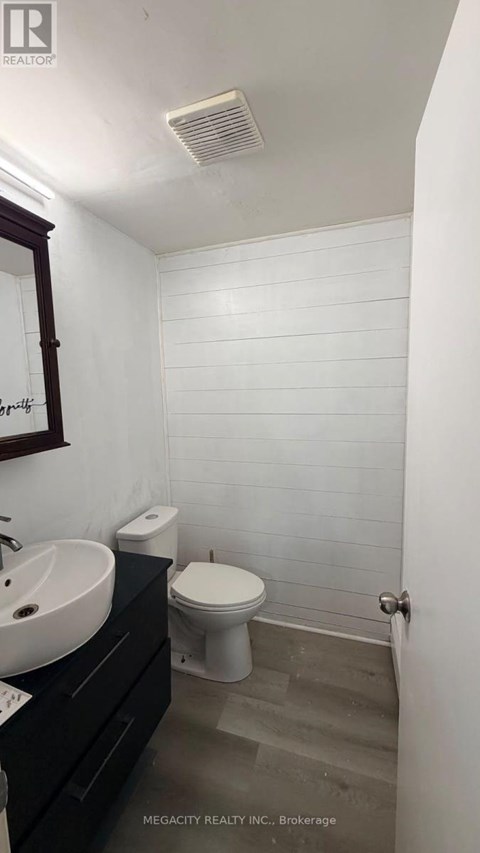 A white tiled bathroom with a toilet, sink, and mirror.