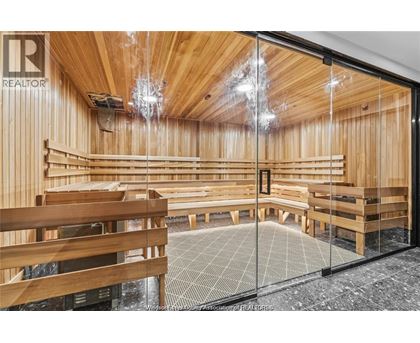 A room with wooden walls and ceiling, furnished with wooden benches and tables, and a glass door leading to a balcony.