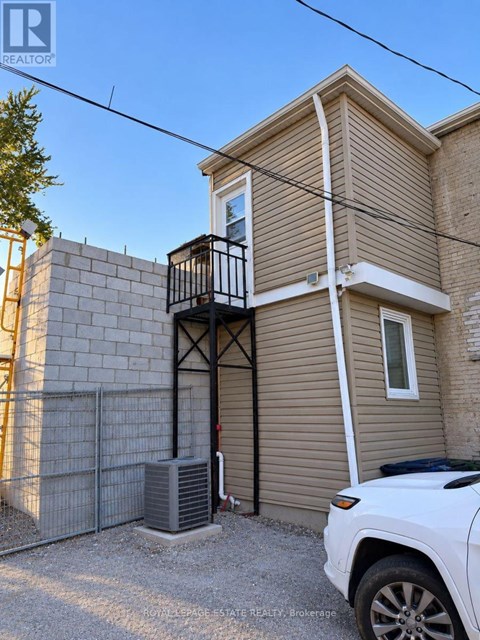 A white car is parked in front of a two-story house with a balcony.